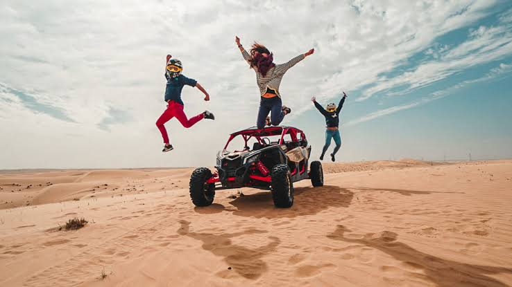 Friends jumping beside a dune buggy in the Dubai desert